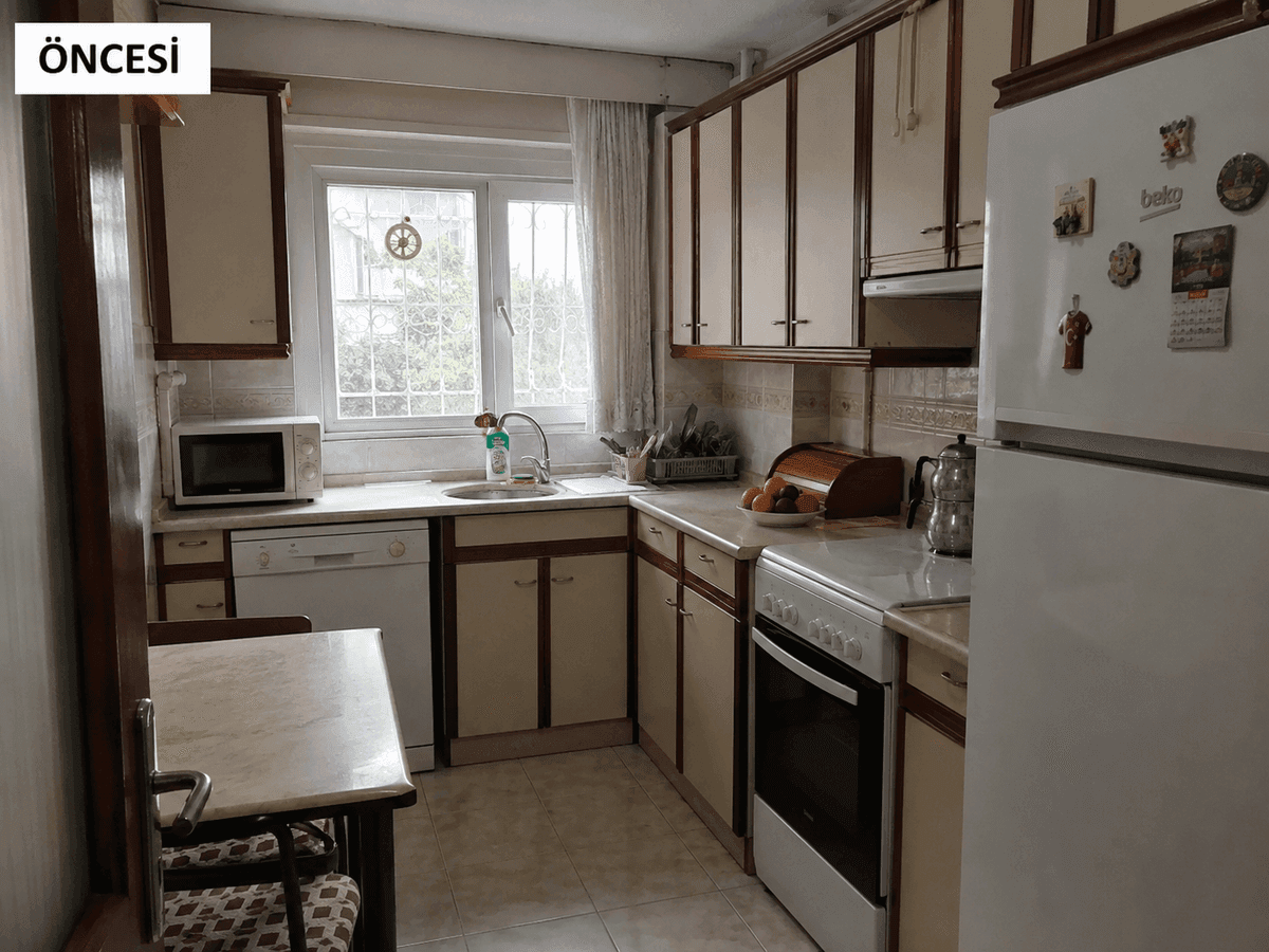 Mersin mutfak dolabı yenileme öncesi — kahverengi çıtalı krem kapaklar, pencere önü lavabo ve beyaz eşyalar